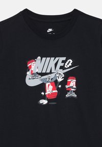 T-shirt en coton noir avec un logo "NIKE" gris et des illustrations de dessins animés, incluant un personnage portant des baskets rouges et un chapeau.