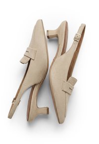 Chaussures slingback beiges en daim avec talons blocs bas, bouts pointus et lanières décoratives sur le cou-de-pied sur fond blanc.