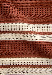 Crochet fabric with alternating horizontal stripes in rust and cream. Features openwork patterns and textured detailing throughout.