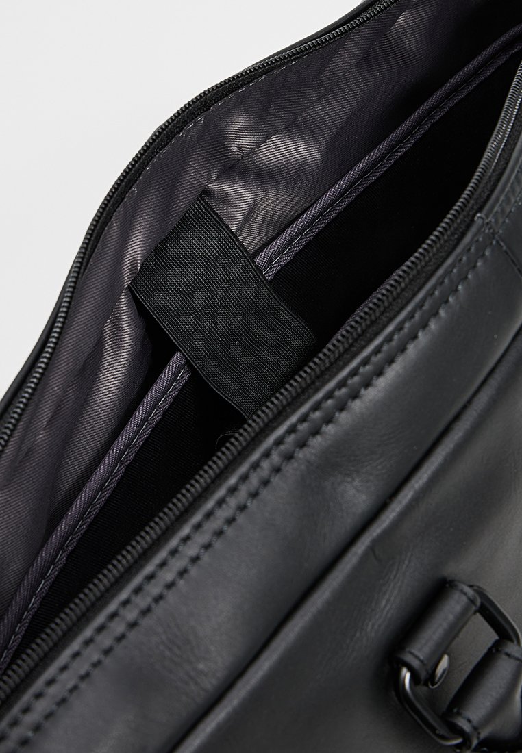 Sac en cuir noir ouvert pour montrer un intérieur doublé avec une sangle élastique noire et une fermeture éclair.