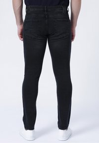 Černé džíny z denimu s úzkým střihem, pěti kapsami a viditelnými zadními kapsami, doplněné bílými teniskami a tmavým tričkem.