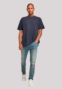 Navy cotton t-shirt with short sleeves, paired with light blue distressed denim jeans and white sneakers. Simple casual design.