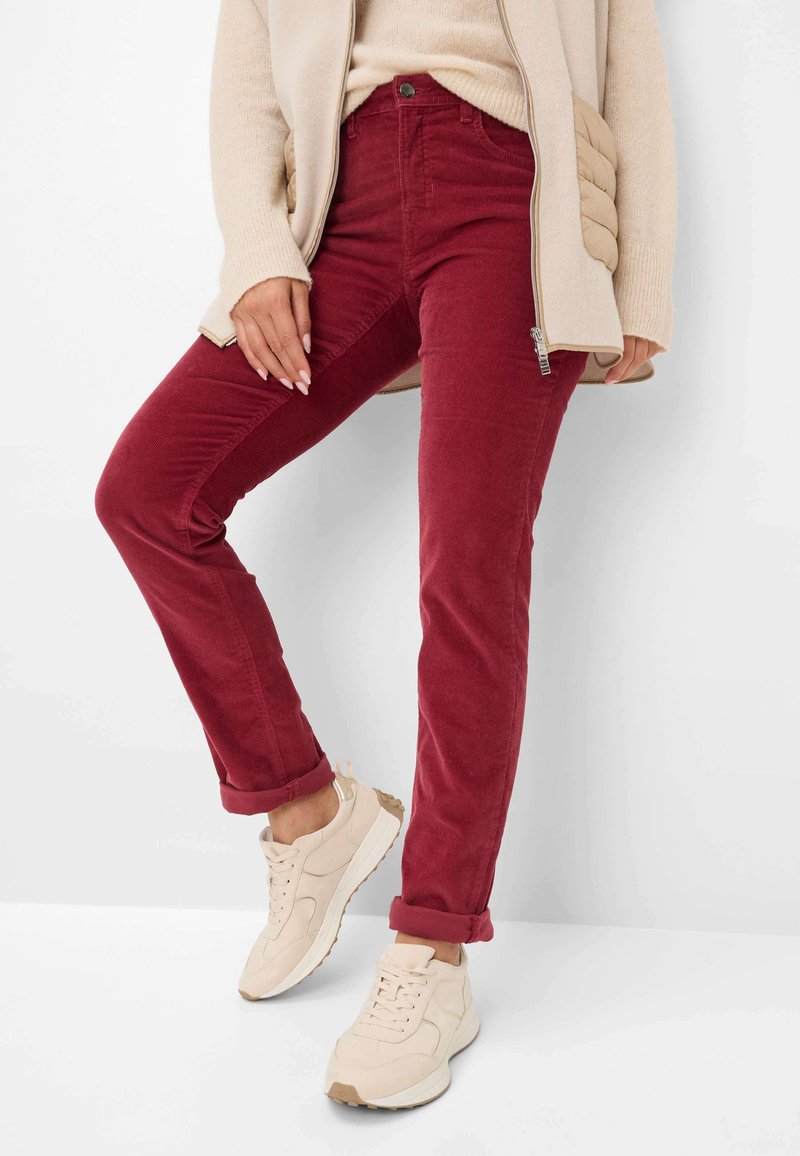 Rode corduroy broek met een slim fit en opgerolde mouwen, gecombineerd met lichtbeige sneakers. De stof heeft een geribbelde textuur.