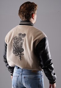 Beige Collegejacke mit schwarzen Lederärmeln; verfügt über ein detailliertes schwarzes Grafikdesign eines Schlanges und TIGERS auf dem Rücken; gerippter Kragen und Bündchen.