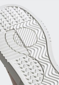 Suela de una zapatilla, con un caucho blanco texturizado que presenta patrones ondulados, áreas circulares y rayadas para un mejor agarre, y un acabado limpio.