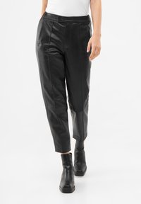 Pantalons en cuir noir avec une coupe ajustée, présentant des coutures avant et un ourlet à revers, complétés par des bottines pour un look audacieux.