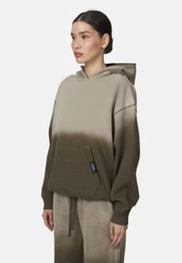 Haut à capuche vert olive avec un design dégradé, poche kangourou et cordon de serrage. Fabriqué dans un tissu doux avec une coupe décontractée.