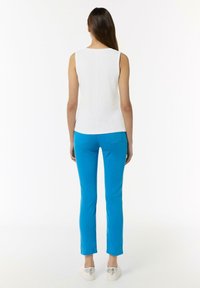 Biała bluzka bez rękawów zestawiona z jaskrawo niebieskimi rurkami. Strój charakteryzuje się gładkim materiałem, prostym krojem i czystymi liniami.