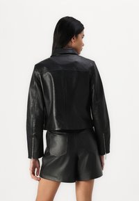 Svart skinnjakke med kort lengde og teksturert mønster, glidelåsede ermer og rett krage, sammen med matchende skinnshorts.