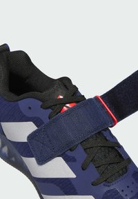Marineblå sportssko med sorte detaljer, tekstureret stof, en velcrorem og reflekterende sølvstriber. Har sorte snørebånd og en mesh-tunge.