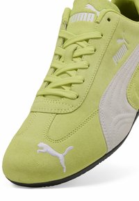 Zapatillas de ante verde claro con marca blanca, acentos texturizados y cordones planos. Presenta una banda lateral blanca contrastante y un logotipo.