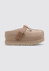 Zoccoli in suede beige con punta rotonda, una fascia in pelle e un elegante carrucola, e suola in gomma testurizzata per una buona aderenza. Design a profilo basso.