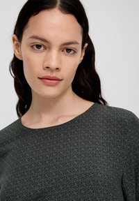 Grünes Oberteil mit einem subtilen, allover Muster aus ineinandergreifenden Formen, rundem Ausschnitt und glatter Textur.