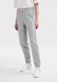 Graue Sweatpants aus Baumwollmischung mit einem Kordelzugbund, Seitentaschen und einem kleinen Logo am linken Oberschenkel. Mit einer glatten Textur akzentuiert.