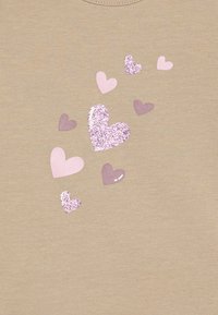 Camisa de algodón beige con corazones en tonos rosa pastel y lavanda de diferentes tamaños, algunos de los cuales están decorados con brillantina.