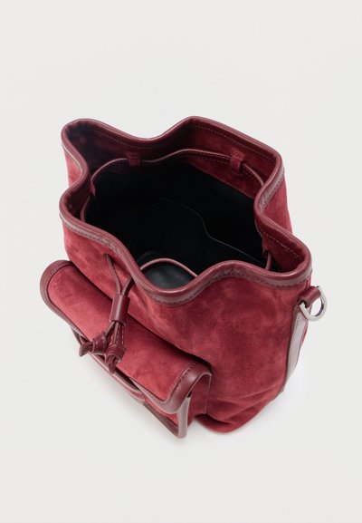 Καπάκι κόκκινης σουέτ τσάντας κουβά με ρυθμιζόμενο κορδόνι, μπροστινή τσέπη και δερμάτινες λεπτομέρειες, εμφανιζόμενο ανοιχτό από πάνω σε λευκό φόντο.