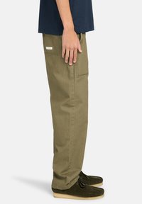 Olijfgroene cargobroek gemaakt van stevig materiaal, met zijzakken en een relaxte pasvorm; gedragen met donkere moccasinschoenen.