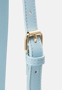 Ljusblå läderrem med guldfärgade detaljer, med en spänne och hål för justering. Slät yta och rena sömmar.
