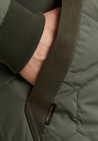 Giacca trapuntata verde con polsini a coste, caratterizzata da un tessuto misto testurizzato e un'etichetta con la dicitura "PME LEGEND" vicino alla chiusura.