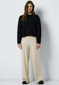 Pulover negru pufos, scurt, asortat cu pantaloni largi bej, având o textură netedă și o cădere subtilă, completat cu pantofi negri.