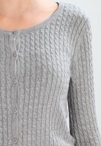 Jasnoszary dziergany kardigan z fakturowanym wzorem warkoczowym, okrągłym dekoltem i pięcioma brązowymi guzikami z przodu.