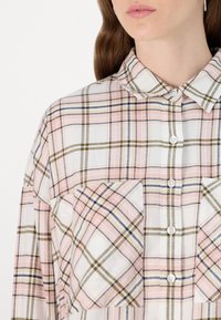 Camisa xadrez em tecido suave, com padrão xadrez em rosa, branco e verde, frente com botões e dois bolsos no peito.