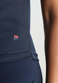 Námořnický sportovní top vyrobený z hladkého materiálu, s malým červeným a šedým logem na straně, s úzkým střihem a plochými švy.