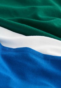 Țesătură verde, albă și albastră cu textură vizibilă și pliuri moi care creează valuri și umbre delicate.