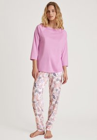Lichtroze top met driekwart mouwen, gecombineerd met witte pyjamabroek met een delicate bloemenprint in roze en marineblauwe tinten.