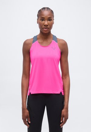 Žena s vrkočmi, oblečená v ružovom športovom tílku bez rukávov so sivými popruhmi a čiernych legínach, stojaca pred jednoduchým svetlým pozadím.