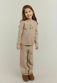 Beige gebreide trui met een kersontwerp, in combinatie met bijpassende losse broek. Bruine instap schoenen met decoratieve studs.