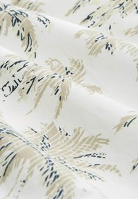 Baumwollstoff mit einem Palmenblattmuster in Beige und Marineblau auf einem weißen Hintergrund, mit einer weichen, glatten Textur.