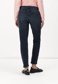Jeans azul oscuro de corte slim, con una cintura de altura media, bolsillos traseros y una textura de denim suave. Combinados con zapatos planos negros.