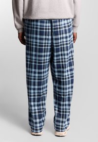 Pantalons à carreaux bleus et bleu clair en tissu doux, avec une coupe décontractée et une jambe droite, présentant des détails de texture subtils.