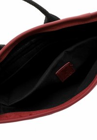 Punainen ja musta olkalaukku, jossa on sileä pinta ja teksturoitu päällinen. Sisäpuoli on mustaa kangasta, ja siinä on nahkainen etiketti sekä tilava lokero.