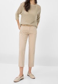 Beige stickad tröja med en lös design, parat med ljusbruna skräddarsydda ankellånga byxor och beige loafers med accentdetaljer.