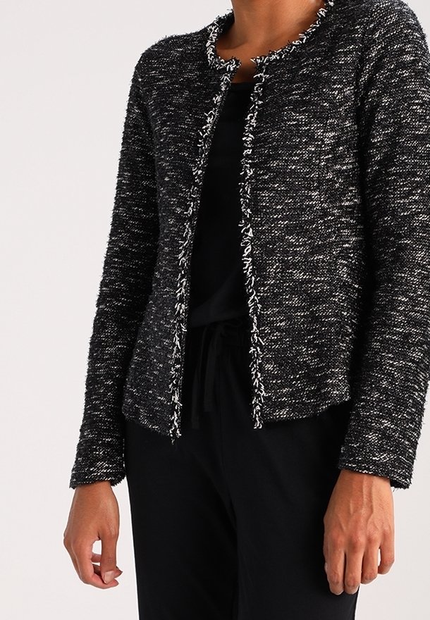 Veste texturée noir et blanc avec un design court, un col rond et des bords effilochés. Présente un devant sans boutons et des manches longues.