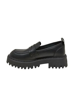 Ben iført sorte og grå argyle knæstrømper med sorte læder loafers på en byfortov nær en åben bildør.
