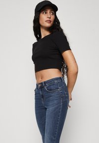 Sort cropped top med korte ærmer, parret med mørkeblå slim-fit jeans med forlommer og knaplukning.