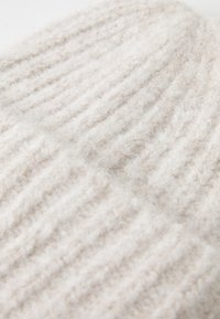 Tejido de punto suave de color crema con una textura esponjosa y un patrón de costillas verticales en primer plano.