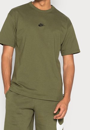 Olijfgroene katoenen T-shirt met een ronde hals, korte mouwen en een klein zwart Nike-logo op de borst. Effen textuur, minimalistisch ontwerp.