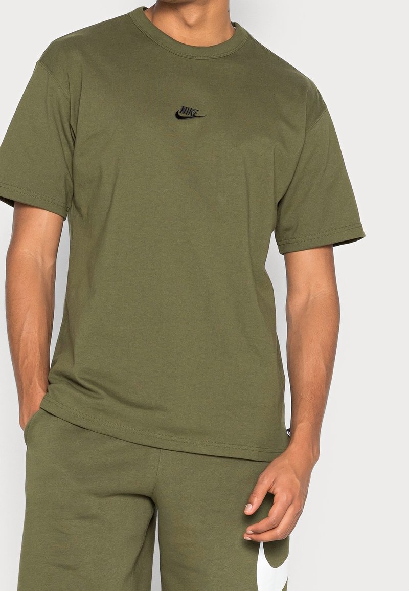 Olivgrön bomull t-shirt med rund halsringning, korta ärmar och en liten svart Nike-logotyp på bröstet. Slät textur, minimal design.