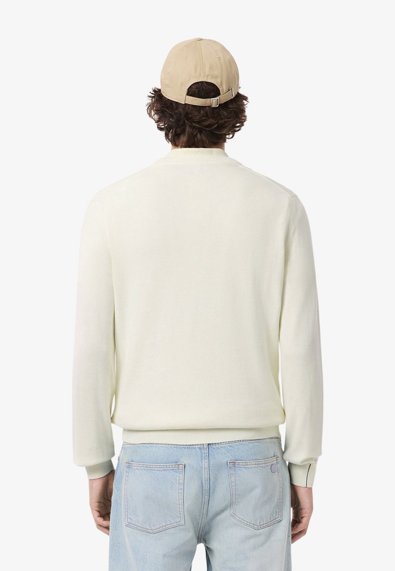 Pull en tricot de couleur claire avec des manches longues, des poignets et un ourlet côtelé. Associé à un jean en denim bleu clair. Casquette de baseball beige.