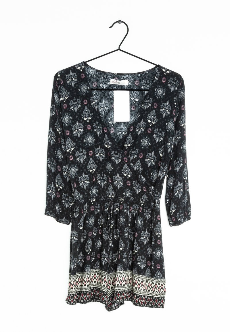 Černý květinový overal s V-výstřihem, tříčtvrtečními rukávy, elastickým pasem a dekorativním lemem s geometrickými vzory na spodním okraji.