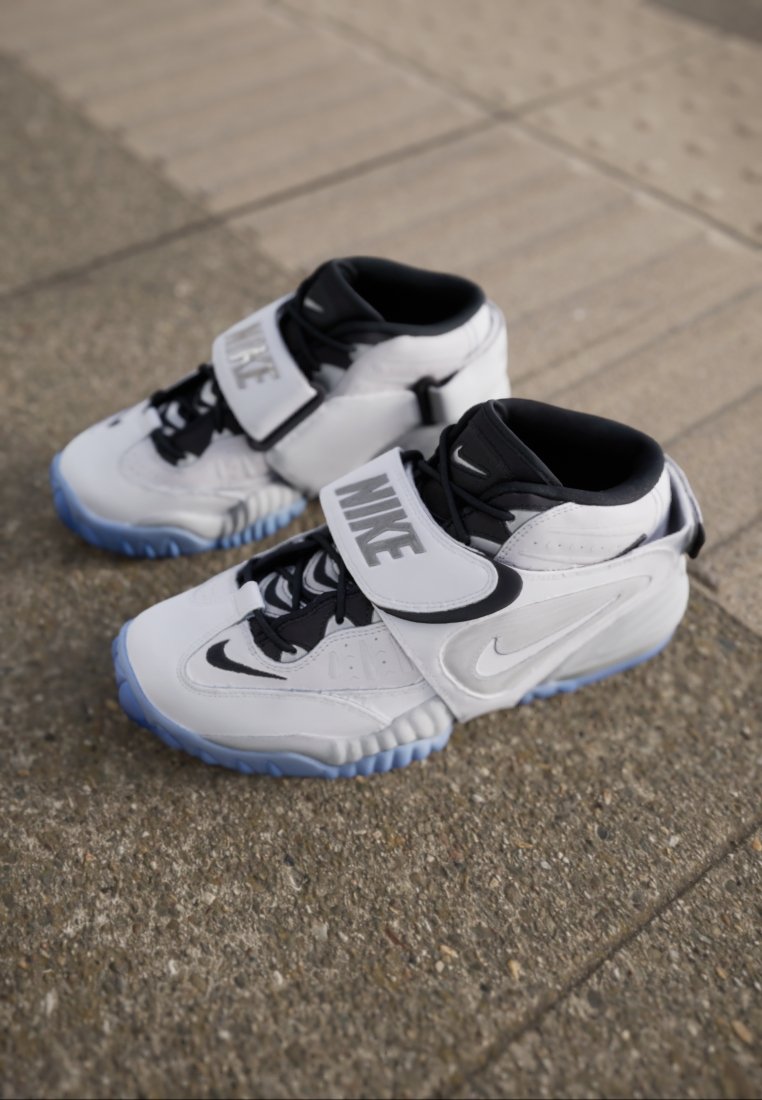 Zapatillas Nike de caña alta, en blanco y negro, con suelas azules, colocadas sobre un pavimento exterior texturizado.