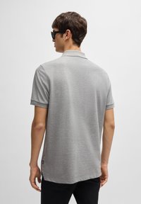 Pelēka īsām piedurknēm polo krekliņš ar klasisku apkakli, smalku tekstūru un sānu spraugām, apvienots ar tumšām biksēm un saulesbrillēm.