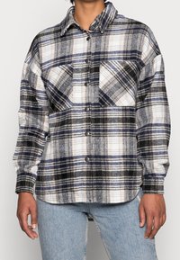 Rutigt flanellskjorta i blått, svart och vitt. Har en knäppning framtill, krage och två bröstfickor. Mjuk textur med lös passform.