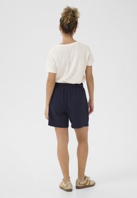 Námornícke modré šortky s elastickým pásom v kombinácii s krémovým tričkom. Outfit dopĺňajú béžové tenisky.