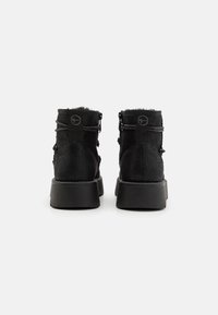 Bottines noires avec une tige en tissu texturé, bout rond et semelle en caoutchouc. Comprend une boucle à l'arrière pour un enfilage facile et des détails de double couture.