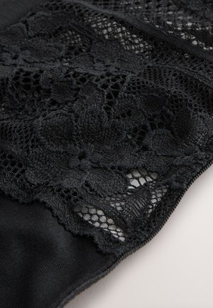 Material de dantelă neagră prezintă modele florale cu secțiuni de țesătură deschisă și închisă, trecând fără întreruperi către un fundal negru solid.